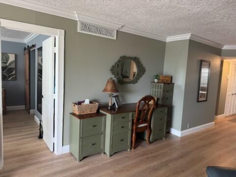 interior space with a barn door, light hardwood / wood-style flooring, a textured ceiling, and ornamental molding