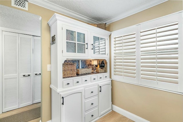 interior space with white cabinetry, light hardwood / wood-style flooring, a textured ceiling, and ornamental molding