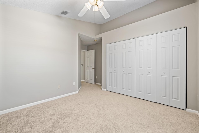 unfurnished bedroom featuring ceiling fan, a closet, light carpet, and a textured ceiling