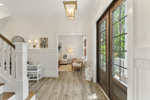 foyer entrance featuring crown molding, french doors, a notable chandelier, and light wood-type flooring