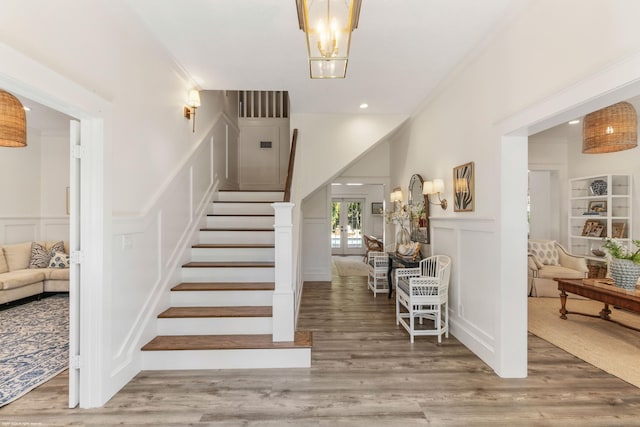 staircase featuring french doors, wood-type flooring, a notable chandelier, and ornamental molding