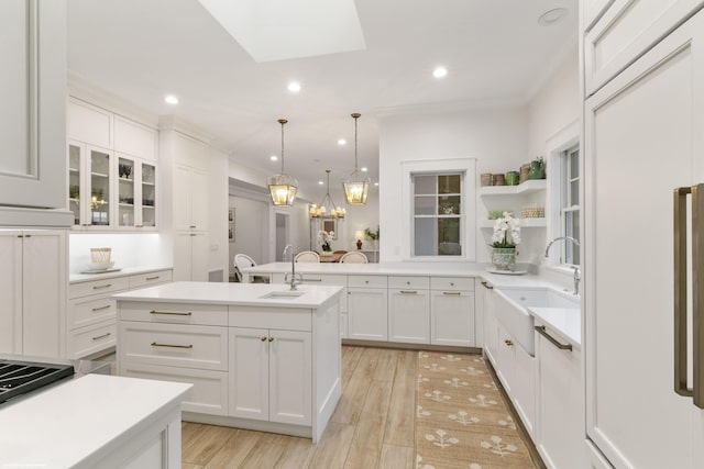 kitchen with a center island with sink, white cabinets, decorative light fixtures, and sink