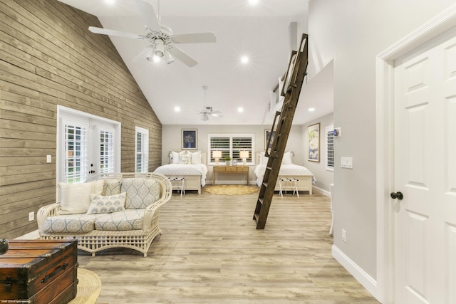 bedroom featuring wood walls, high vaulted ceiling, french doors, light hardwood / wood-style flooring, and ceiling fan