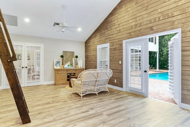 sitting room with ceiling fan, french doors, wood walls, light hardwood / wood-style floors, and vaulted ceiling