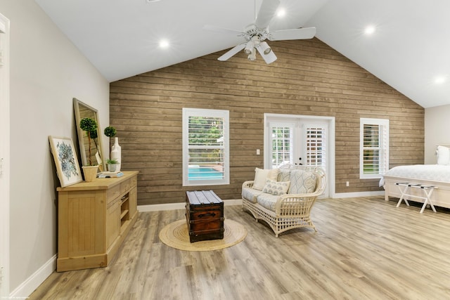 sitting room with ceiling fan, french doors, high vaulted ceiling, wood walls, and light wood-type flooring