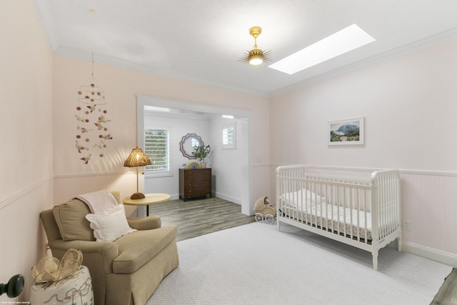 bedroom with a skylight, crown molding, hardwood / wood-style floors, and a crib