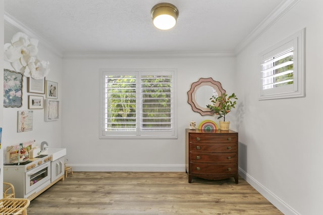 interior space with light wood-type flooring, a textured ceiling, and ornamental molding