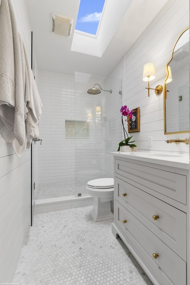 bathroom featuring a skylight, vanity, tiled shower, tile patterned flooring, and toilet