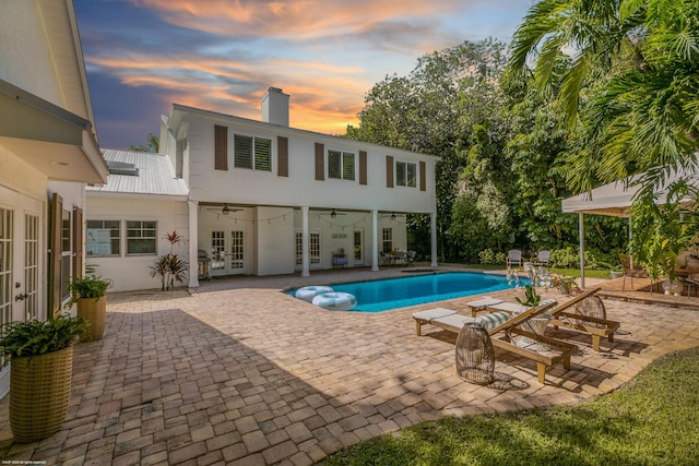 pool at dusk featuring a patio area, ceiling fan, and french doors