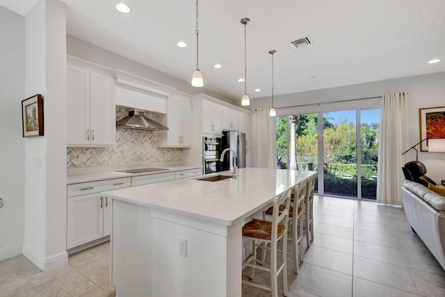 kitchen featuring white cabinets, a center island with sink, and wall chimney range hood