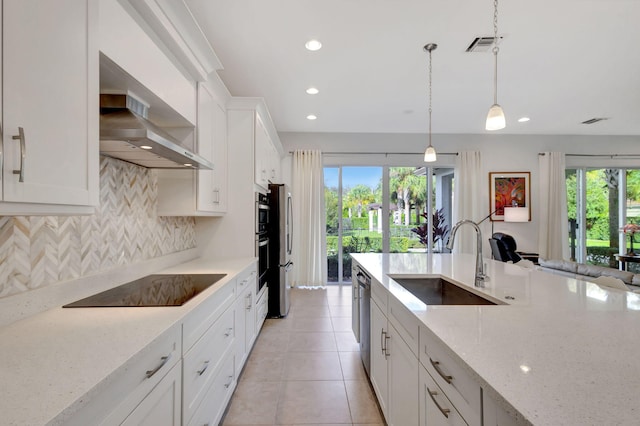 kitchen with light stone counters, black electric cooktop, sink, pendant lighting, and white cabinets