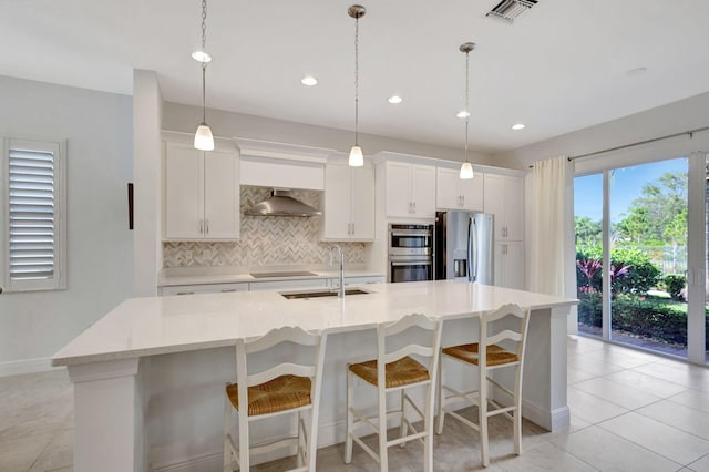 kitchen featuring white cabinetry, wall chimney exhaust hood, a kitchen island with sink, and appliances with stainless steel finishes