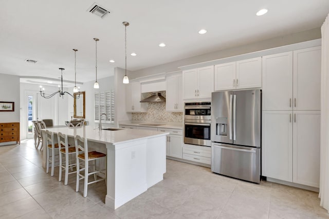 kitchen with sink, wall chimney range hood, a kitchen island with sink, white cabinets, and appliances with stainless steel finishes