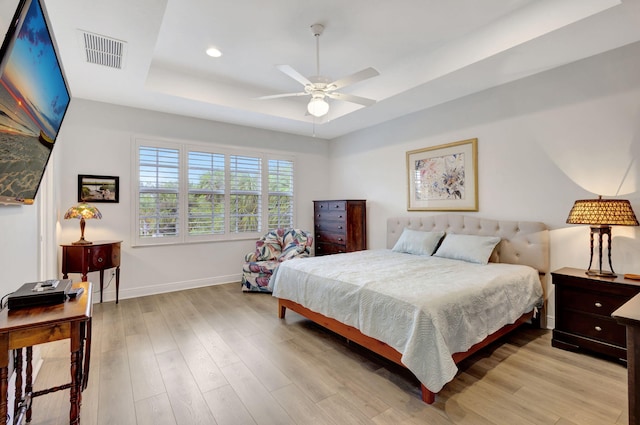 bedroom featuring ceiling fan, light hardwood / wood-style flooring, and a tray ceiling