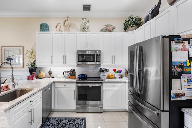 kitchen with sink, light tile patterned floors, light stone countertops, appliances with stainless steel finishes, and white cabinetry