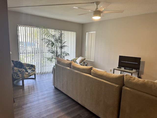 living room with a textured ceiling, ceiling fan, and dark wood-type flooring