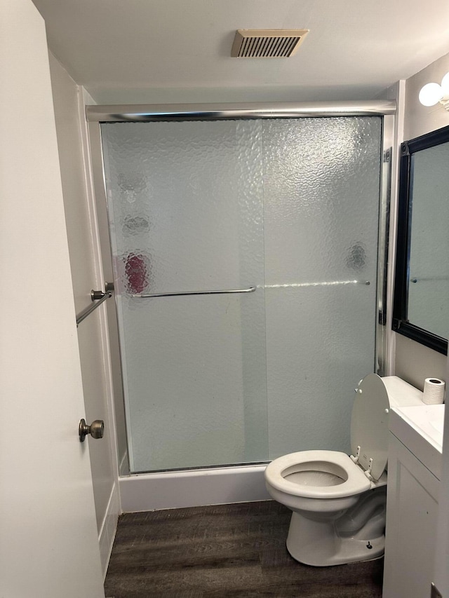 bathroom featuring hardwood / wood-style floors, vanity, a shower with shower door, and toilet