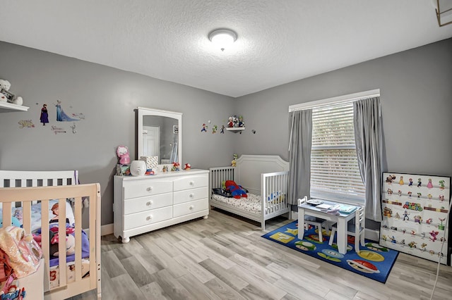 bedroom featuring light hardwood / wood-style flooring, a nursery area, and a textured ceiling