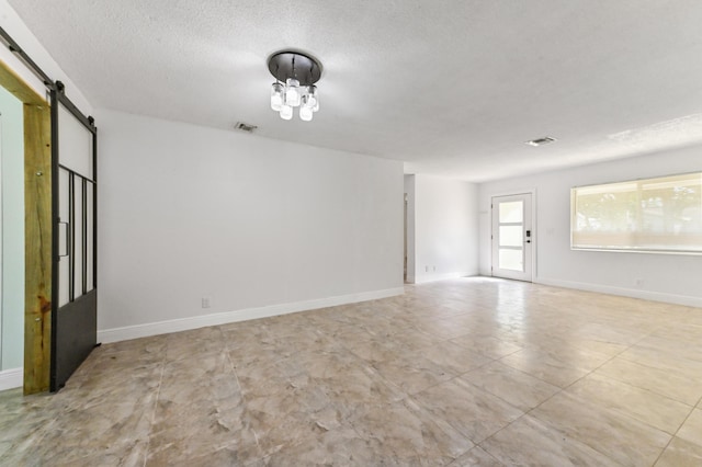 unfurnished room with a barn door and a textured ceiling