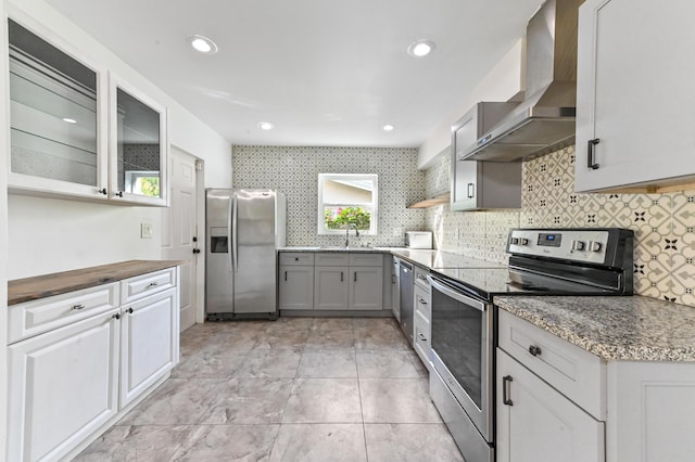 kitchen featuring gray cabinetry, wall chimney range hood, sink, decorative backsplash, and appliances with stainless steel finishes