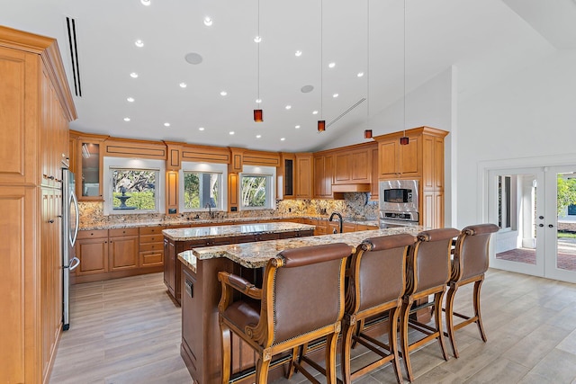 kitchen with appliances with stainless steel finishes, light stone counters, a healthy amount of sunlight, a spacious island, and a breakfast bar area