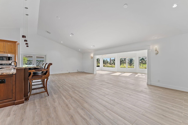 kitchen with light stone countertops, stainless steel microwave, a kitchen breakfast bar, high vaulted ceiling, and light wood-type flooring