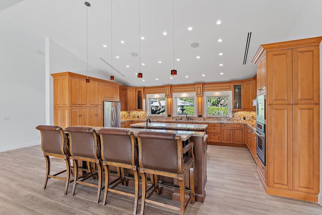 kitchen with light stone countertops, appliances with stainless steel finishes, a spacious island, light hardwood / wood-style flooring, and hanging light fixtures