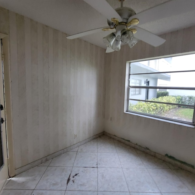 unfurnished room featuring light tile patterned floors, ceiling fan, and wood walls