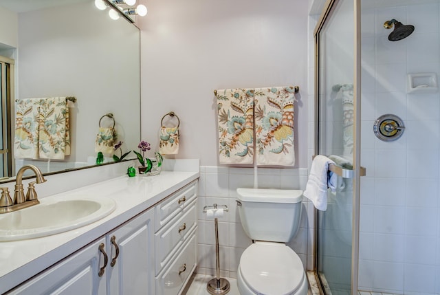 bathroom with vanity, toilet, a shower with shower door, and tile walls