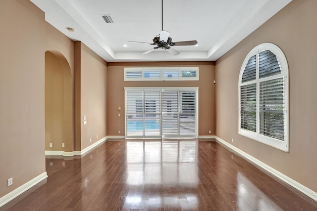 empty room with dark hardwood / wood-style floors, a raised ceiling, and ceiling fan