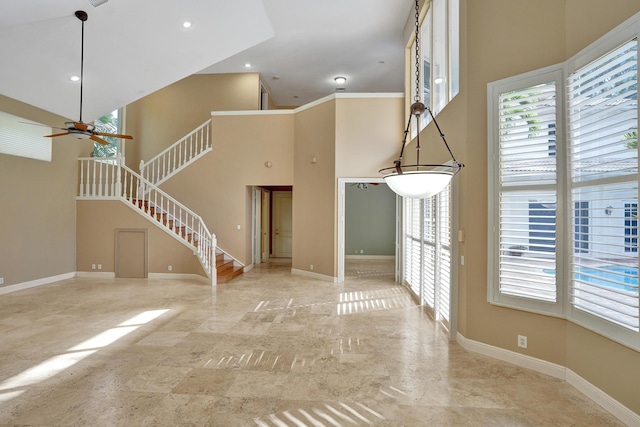 unfurnished living room with ceiling fan, a towering ceiling, and crown molding