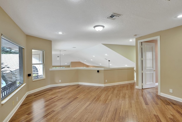 additional living space with light wood-type flooring, a textured ceiling, and vaulted ceiling