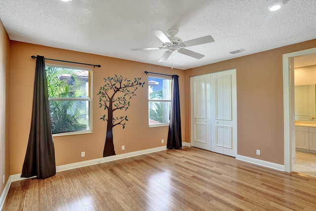 unfurnished bedroom with ensuite bathroom, ceiling fan, light wood-type flooring, multiple windows, and a closet