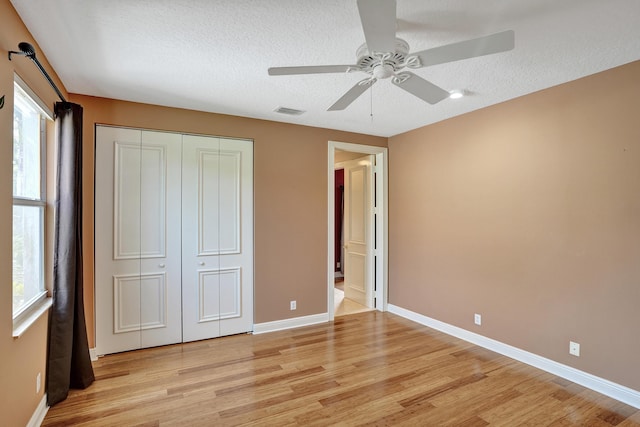 unfurnished bedroom featuring ceiling fan, a closet, a textured ceiling, and light hardwood / wood-style flooring