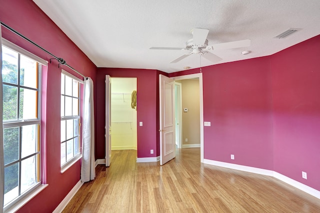 unfurnished room featuring ceiling fan, a healthy amount of sunlight, light wood-type flooring, and a textured ceiling