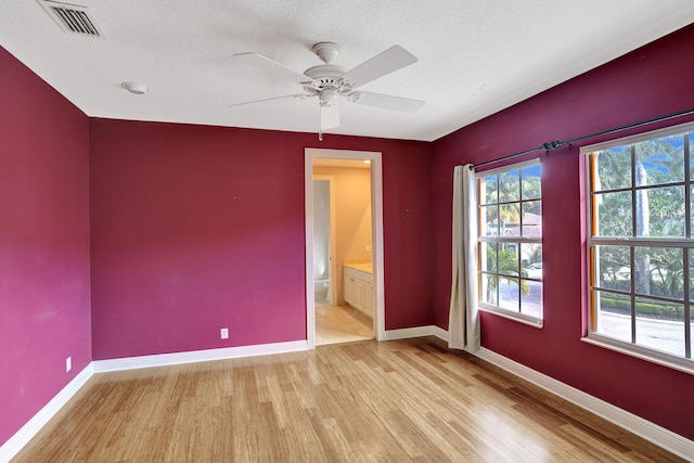 unfurnished bedroom with a textured ceiling, ensuite bathroom, light hardwood / wood-style flooring, and ceiling fan