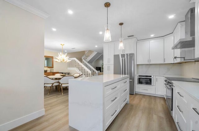 kitchen with stainless steel appliances, a kitchen island, wall chimney range hood, pendant lighting, and white cabinetry