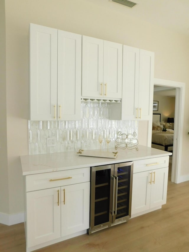 bar with light wood-type flooring, decorative backsplash, beverage cooler, and a dry bar