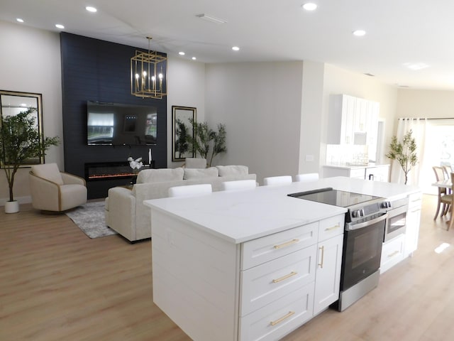 kitchen featuring stainless steel electric range oven, pendant lighting, a fireplace, white cabinets, and light stone counters