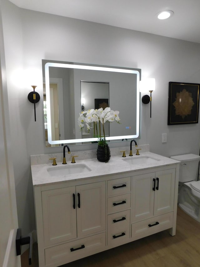 full bathroom featuring double vanity, wood finished floors, toilet, and a sink