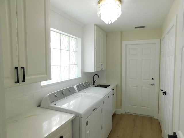 clothes washing area with visible vents, light wood-style flooring, cabinet space, a sink, and washer and dryer