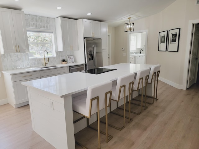 kitchen with tasteful backsplash, washing machine and dryer, light wood-type flooring, appliances with stainless steel finishes, and a sink