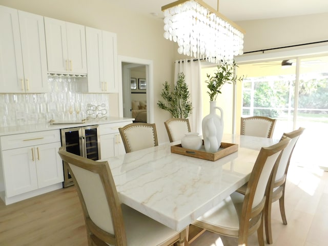 dining area with wine cooler, light wood-style flooring, bar area, and an inviting chandelier