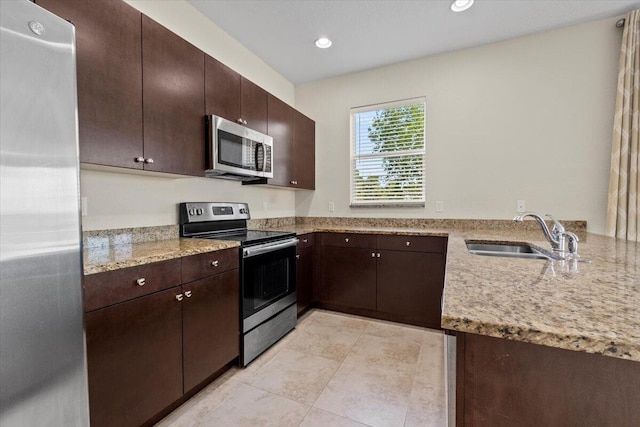 kitchen featuring light stone countertops, appliances with stainless steel finishes, kitchen peninsula, dark brown cabinets, and sink