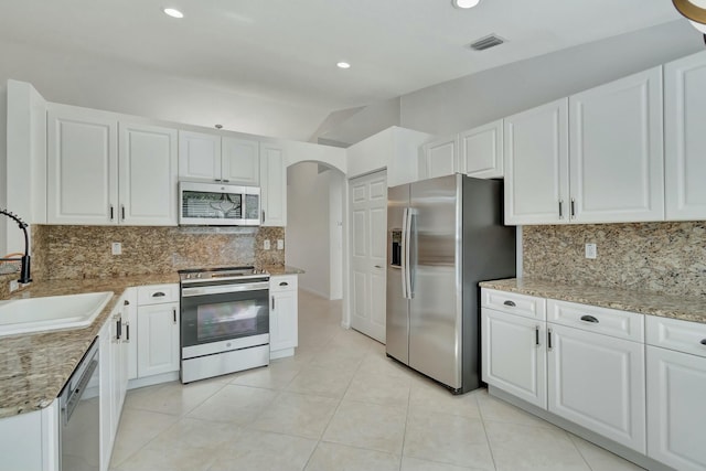 kitchen with stainless steel appliances, vaulted ceiling, sink, light tile patterned floors, and white cabinets