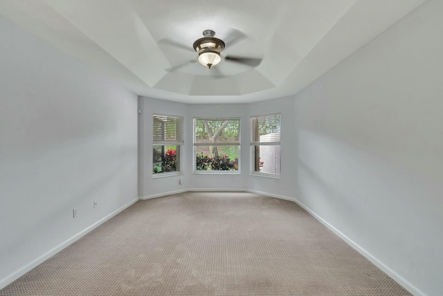 carpeted empty room featuring ceiling fan and a raised ceiling