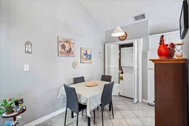 tiled dining room featuring stacked washer / drying machine, lofted ceiling, and a textured ceiling