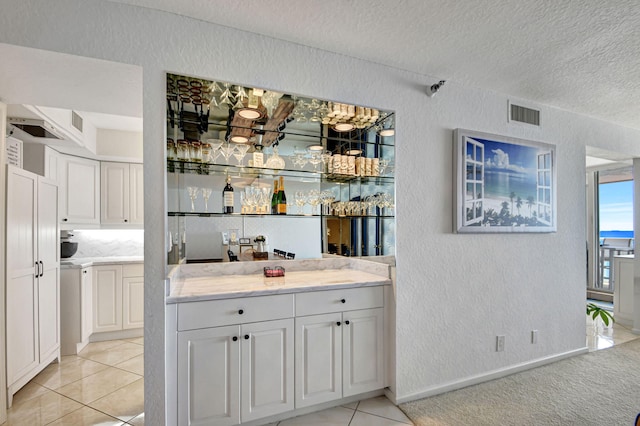 bar featuring a textured ceiling, light colored carpet, and white cabinetry