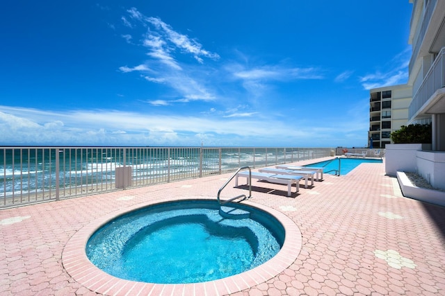 view of swimming pool featuring a community hot tub, a water view, and a beach view