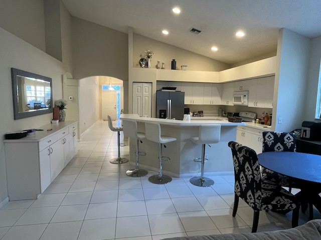 kitchen featuring a kitchen breakfast bar, white cabinetry, light tile patterned flooring, and white appliances